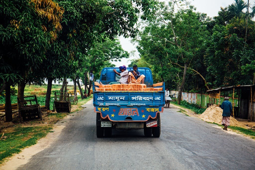 A vibrant truck carries passengers and goods on a rural road with lush greenery.